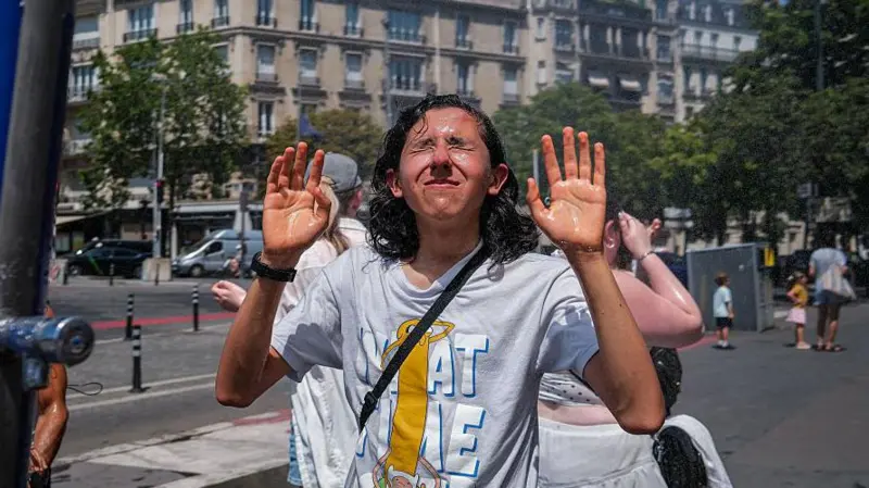 Visitantes resguardándose del sol con sombrillas frente a la estructura de vidrio del Museo del Louvre durante un día soleado.