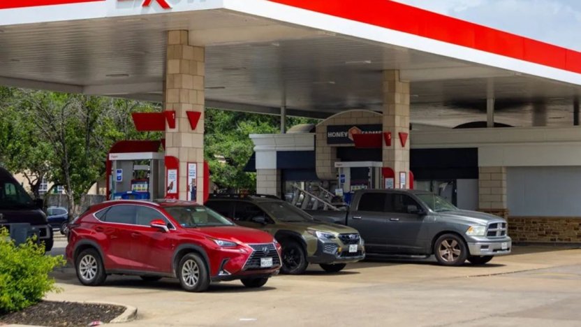 Una manguera de combustible colocada en el tanque de un automóvil en una gasolinera estadounidense con los precios digitales de fondo.