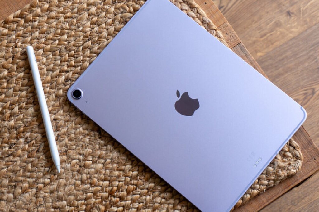 Vista frontal de una tableta iPad con pantalla encendida mostrando la interfaz de inicio junto a un Apple Pencil sobre un escritorio, representando los dispositivos iPad de Apple.