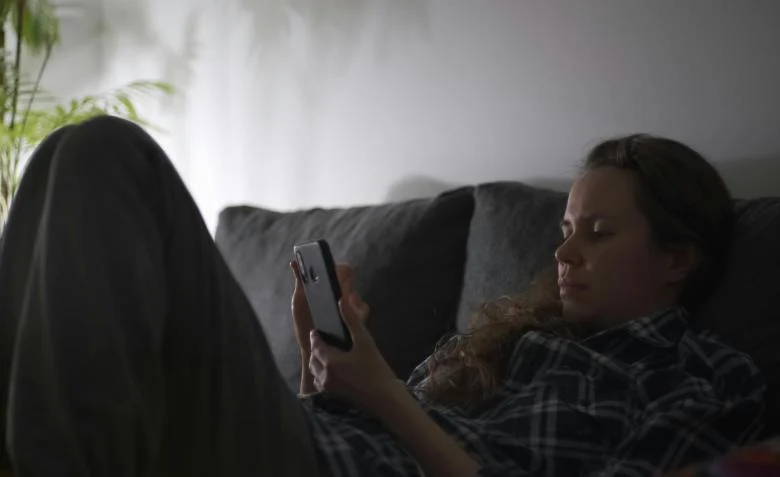 Mujer utilizando un chatbot en su teléfono para recibir apoyo emocional, con un psicólogo supervisando la interacción en segundo plano.