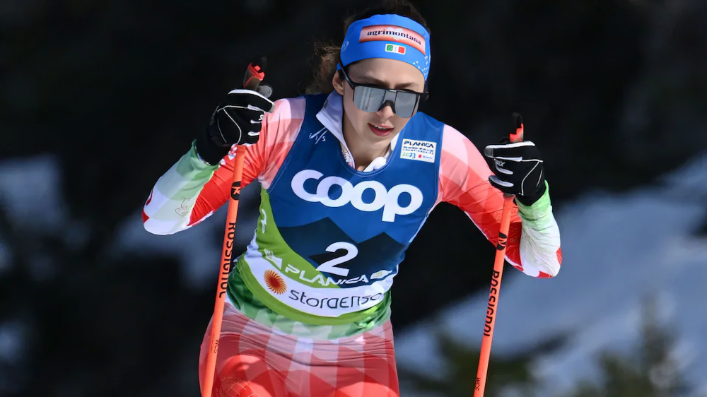 Regina Martínez con traje de esquí y bandera mexicana en la pista de los Juegos Olímpicos de Invierno, lista para competir.