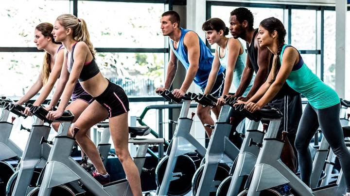 Grupo de personas disfrutando una clase de spinning en un gimnasio, pedaleando con entusiasmo y energía.