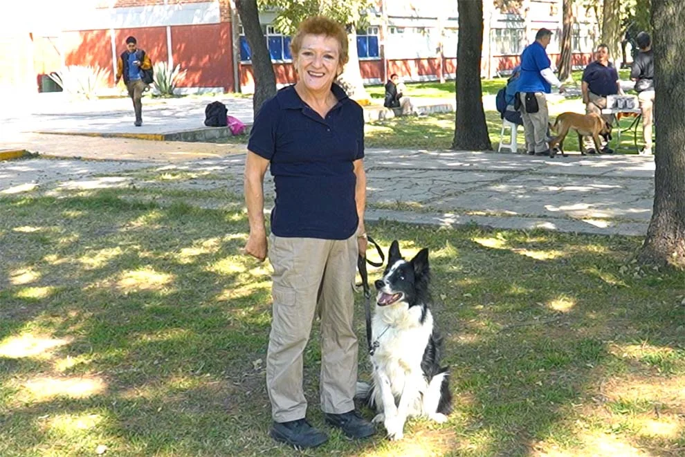 Adulto mayor sonriendo mientras pasea a su perro en un parque soleado.