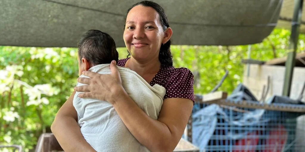 Familia sonriendo frente a su nueva casa mejorada, símbolo de vivienda digna y salud.