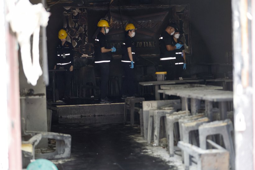 Investigadores policiales inspeccionando el interior calcinado y las mesas cubiertas de ceniza tras el incendio en un bar de Bangkok.