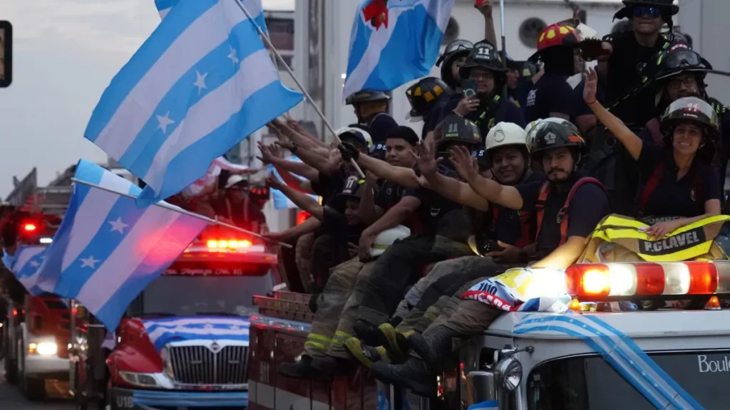 Formación de bomberos ecuatorianos con uniformes de parada rindiendo honores en ceremonia cívica