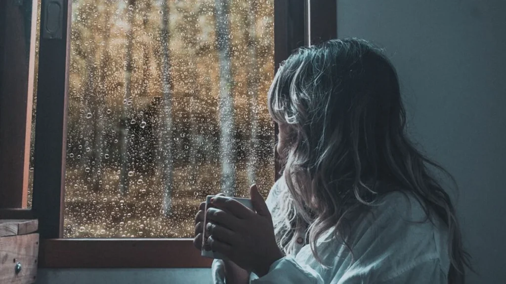 Persona contemplando gotas de lluvia a través de una ventana iluminada con calma